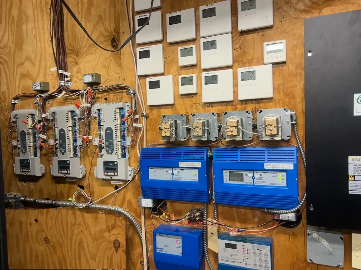 Thermostats, blue heating controllers, and open control panels with wiring mounted on a plywood board.