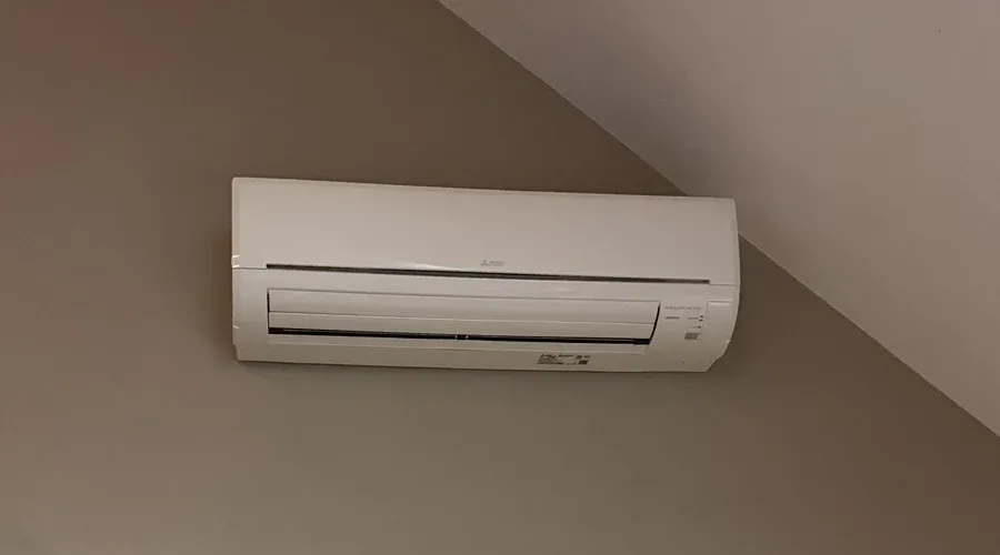 White ductless indoor unit mounted on a beige wall beneath a sloped ceiling.